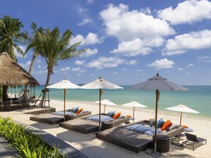 A beachside lounge area with sunbeds, umbrellas, and a thatched structure. - Mercure Samui Chaweng Tana Hotel (Koh Samui)