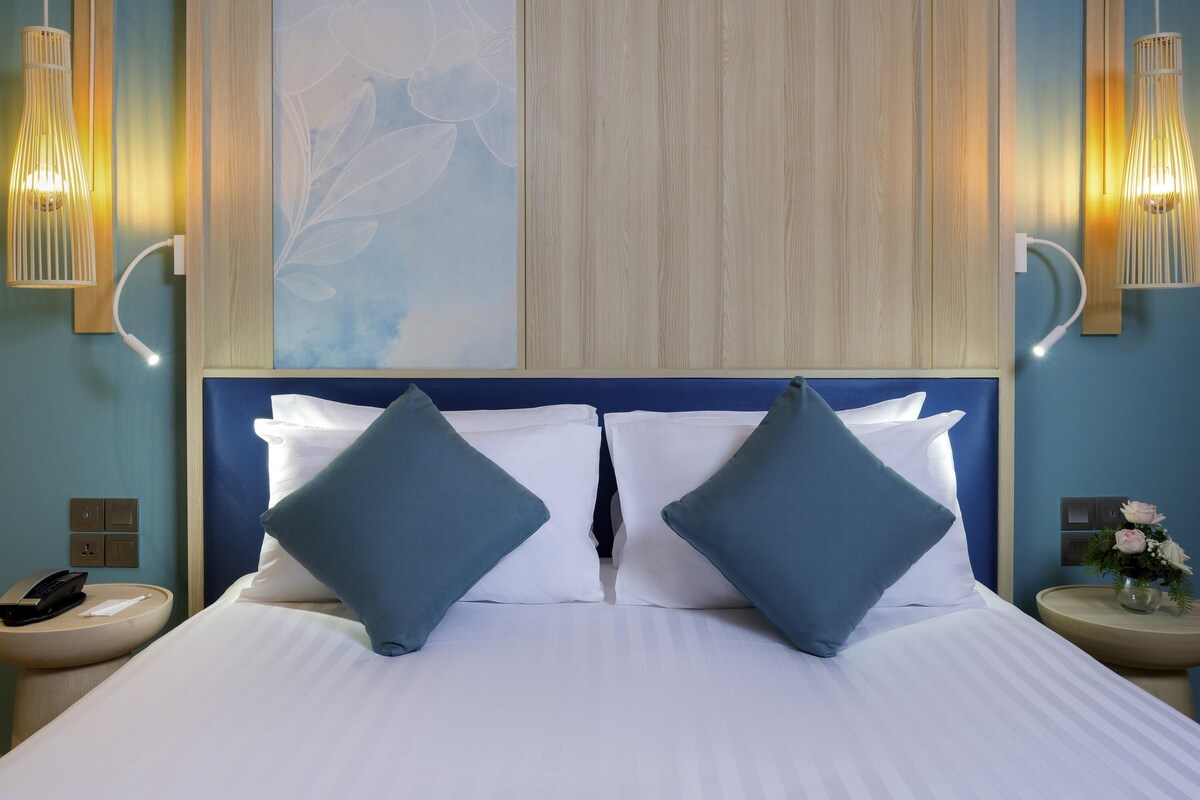 A hotel room with a bed, two wall-mounted lamps, a nightstand with a phone, and a wall art piece.