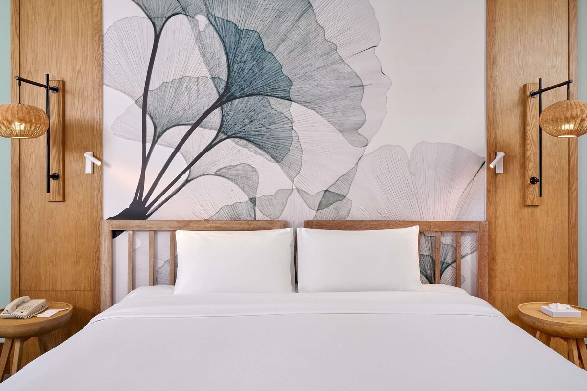 Habitación de hotel con una cama grande, dos mesitas de noche, un teléfono en la pared y una obra de arte floral abstracta de gran tamaño.
