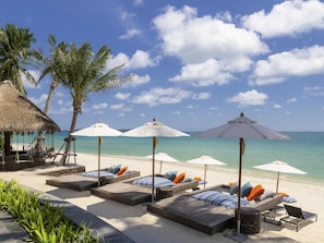 A beachside lounge area with sunbeds, umbrellas, and a thatched structure.