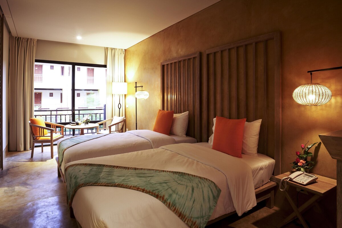 A hotel room with a bed, a desk with a telephone, a chair, a lamp, and a view of the outside.