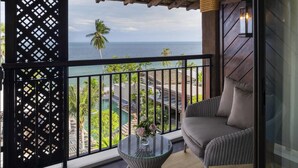 Un balcón con vista al mar, una silla de mimbre, una mesita con un jarrón y techo de madera.