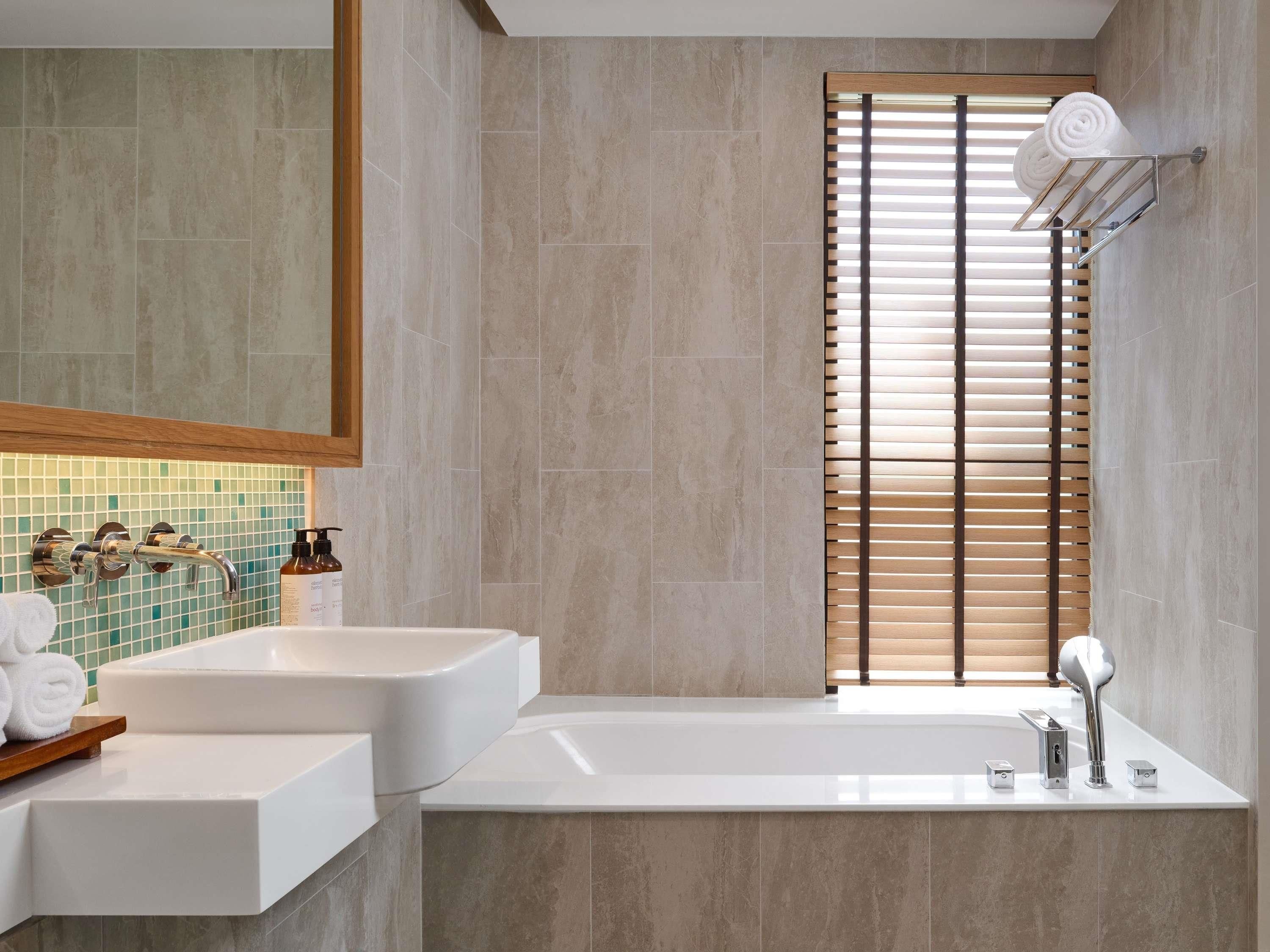 A modern bathroom with two sinks, a large mirror, and a window with blinds.