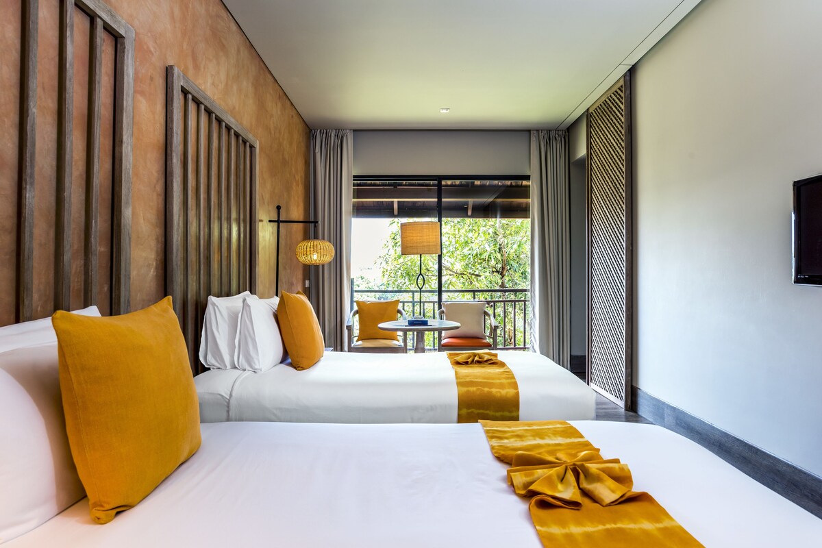 A hotel room with two beds, a balcony, and a view of greenery.