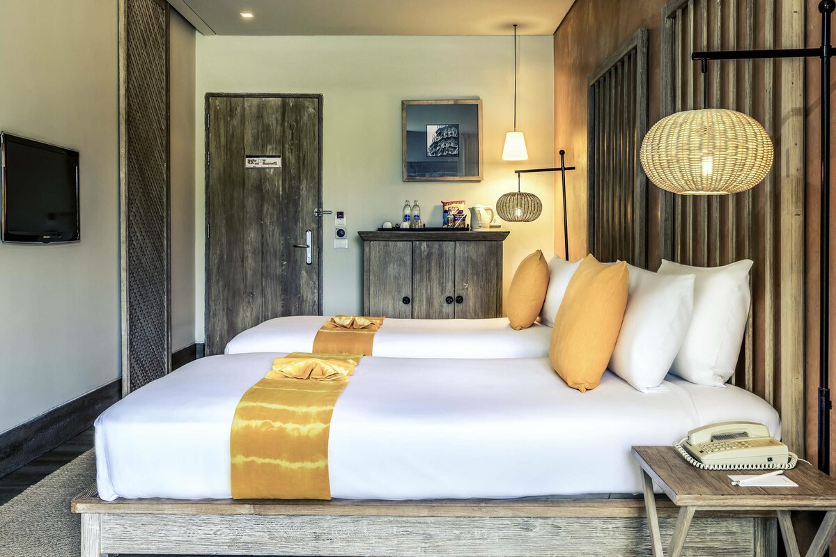 A hotel room with a bed, bedside table, lamp, and a television mounted on the wall.
