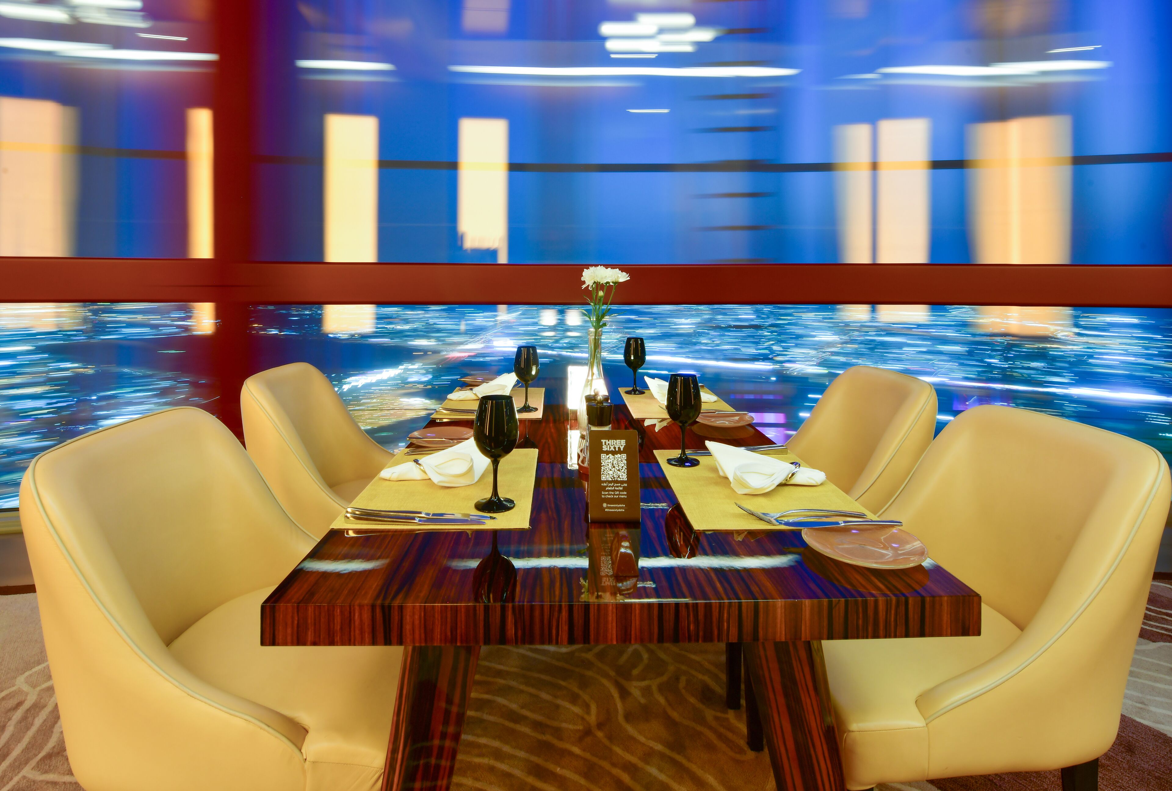 A dining table set for four with a view of a water body through a large window.
