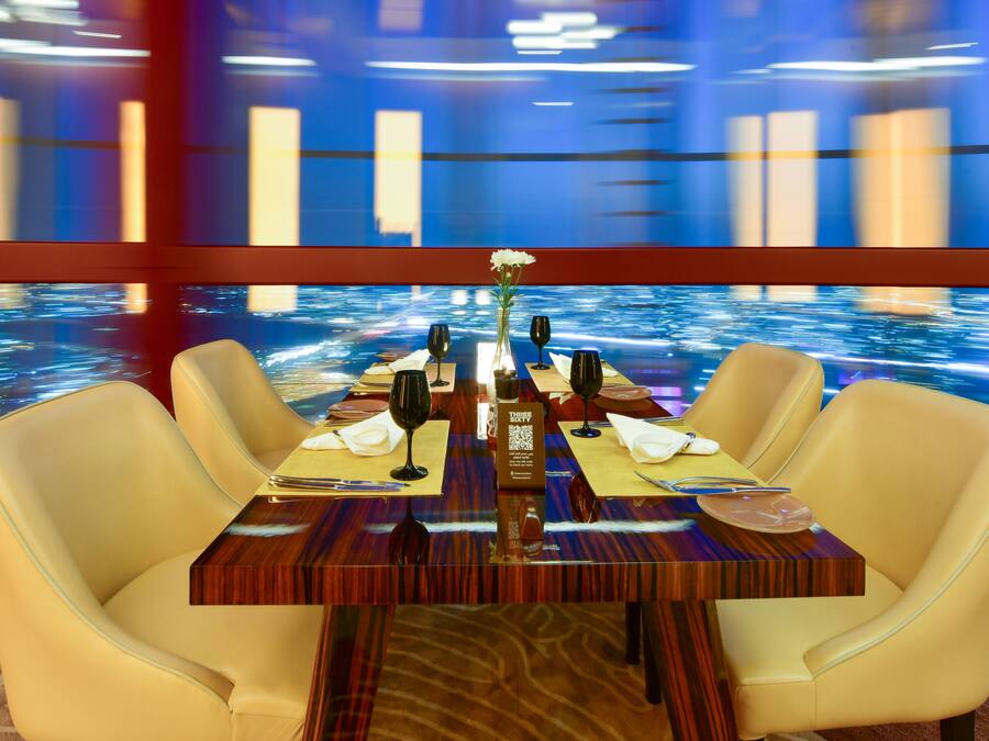 A dining table set for four with a view of a water body through a large window.