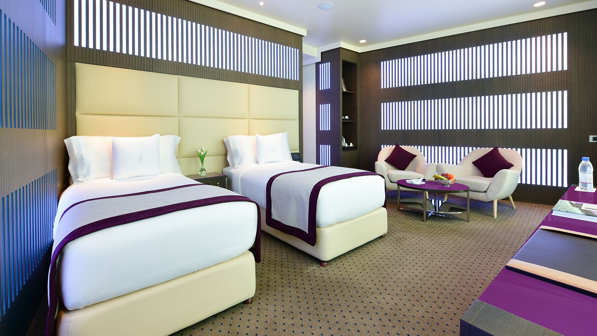 A hotel room with two beds, a sofa, a coffee table, and a minibar.