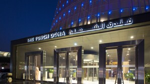 Een modern gebouw met glazen deuren en een bord waarop 'The Torch Doha' staat.