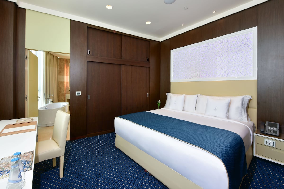 A hotel room with a large bed, a desk with a chair, a vanity with a mirror, and a large window with a decorative view.