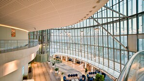 Een moderne hotel lobby met een gebogen plafond, grote ramen en een zithoek met banken en tafels.