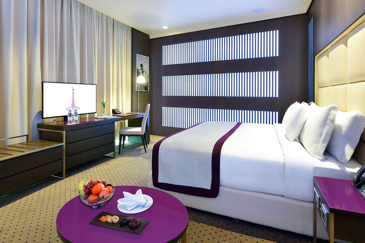 A modern hotel room with a bed, desk, and a small table with fruit.