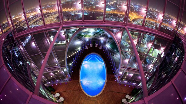Panoramisch uitzicht vanaf een hoog hotel, met een grote glazen atrium, een fontein en een stadsgezicht 's nachts.