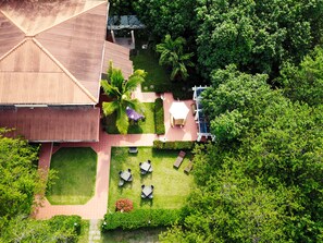 Vista aérea de una propiedad con un edificio grande, un patio con mesas y sillas, y vegetación circundante.