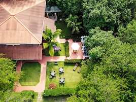 Vista aérea de una propiedad con un edificio grande, un patio con mesas y sillas, y vegetación circundante.