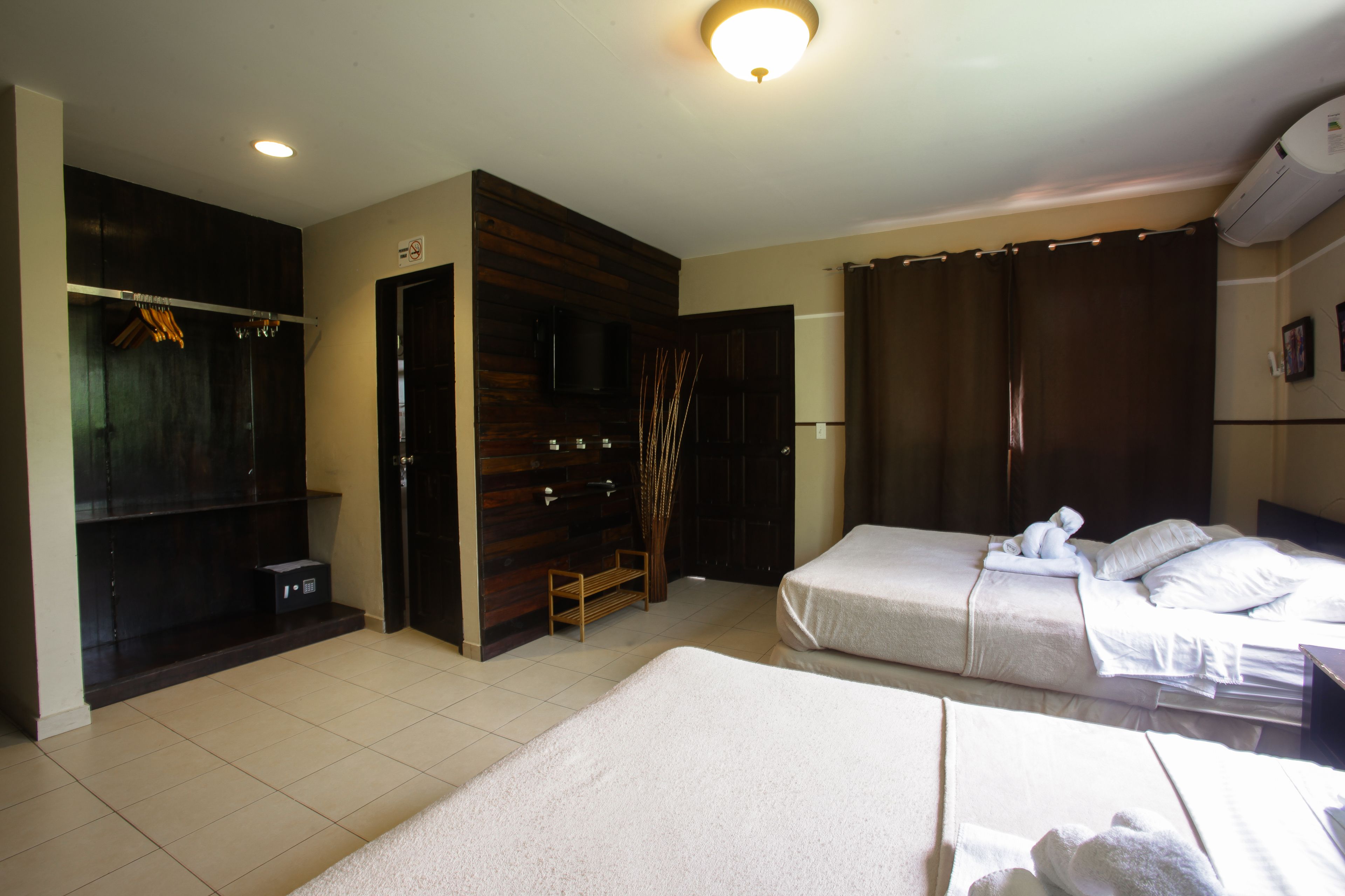 A hotel room with two beds, a wardrobe, a television, and a shower area.