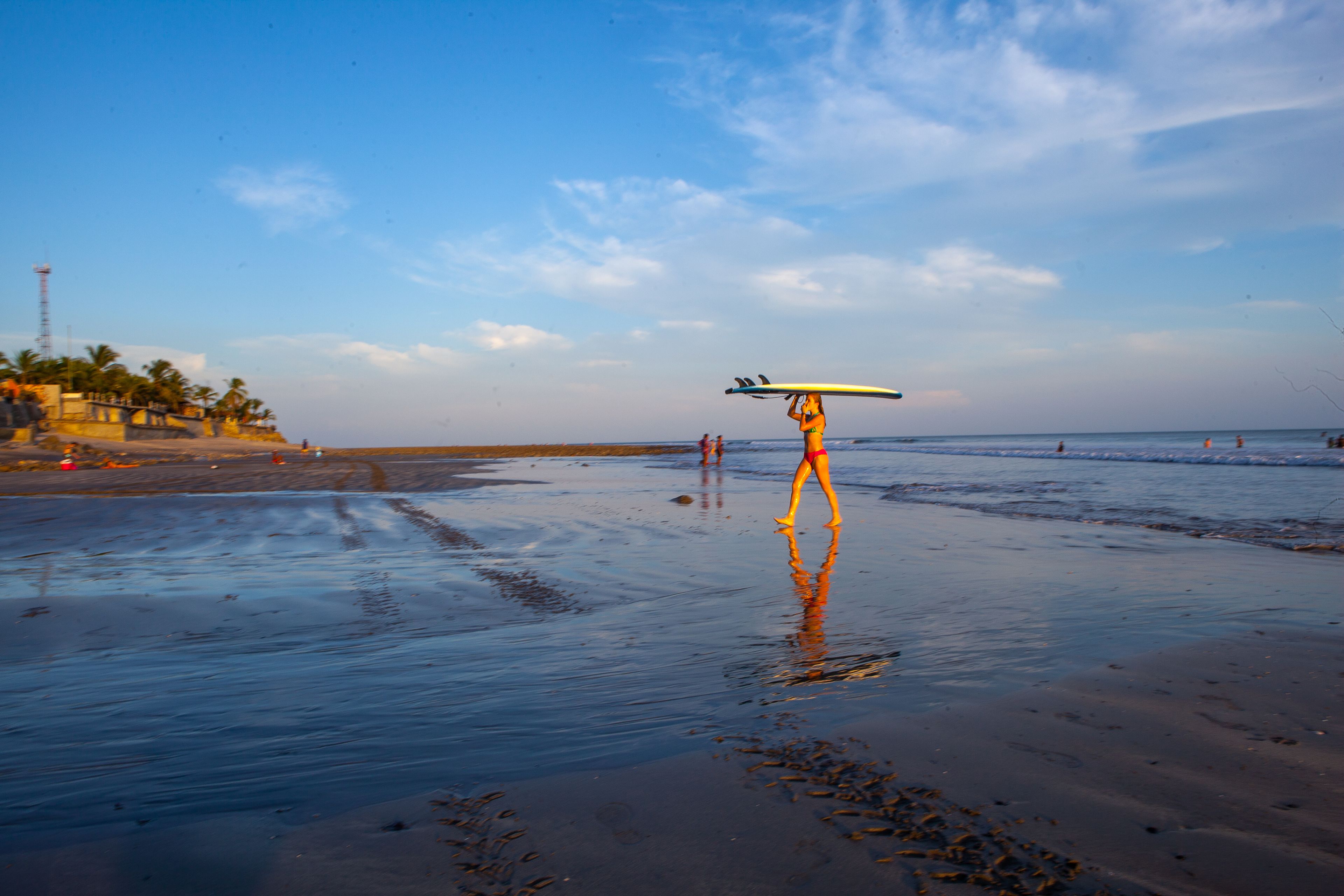 A beach scene with a person carrying a surfboard.