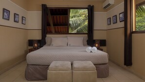 A bedroom with a bed, two bedside tables, a window with curtains, and a wall-mounted air conditioner. - Manglar Lodge (San Carlos)