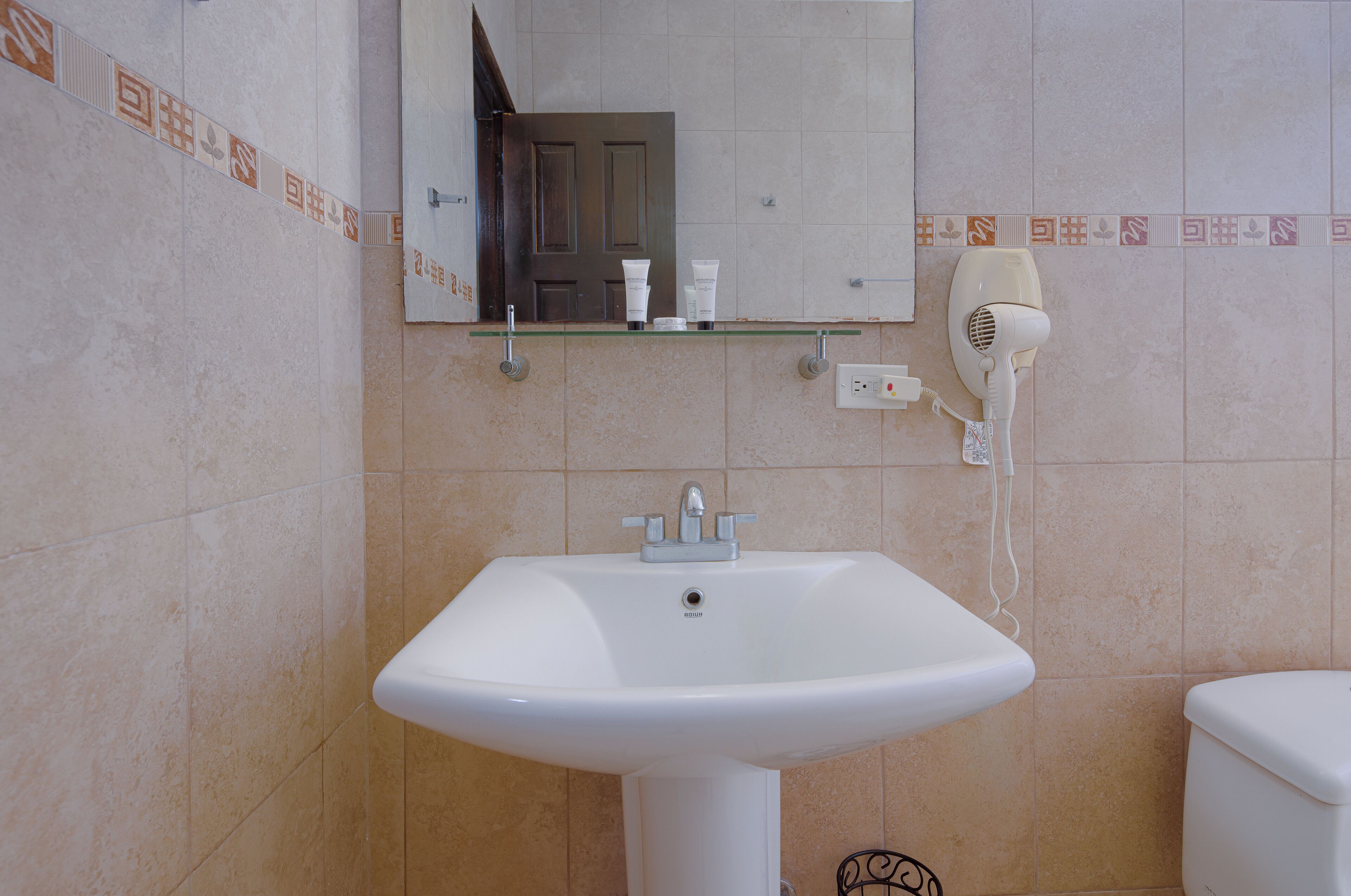 A bathroom with a white sink, a mirror, and a hairdryer on the wall.