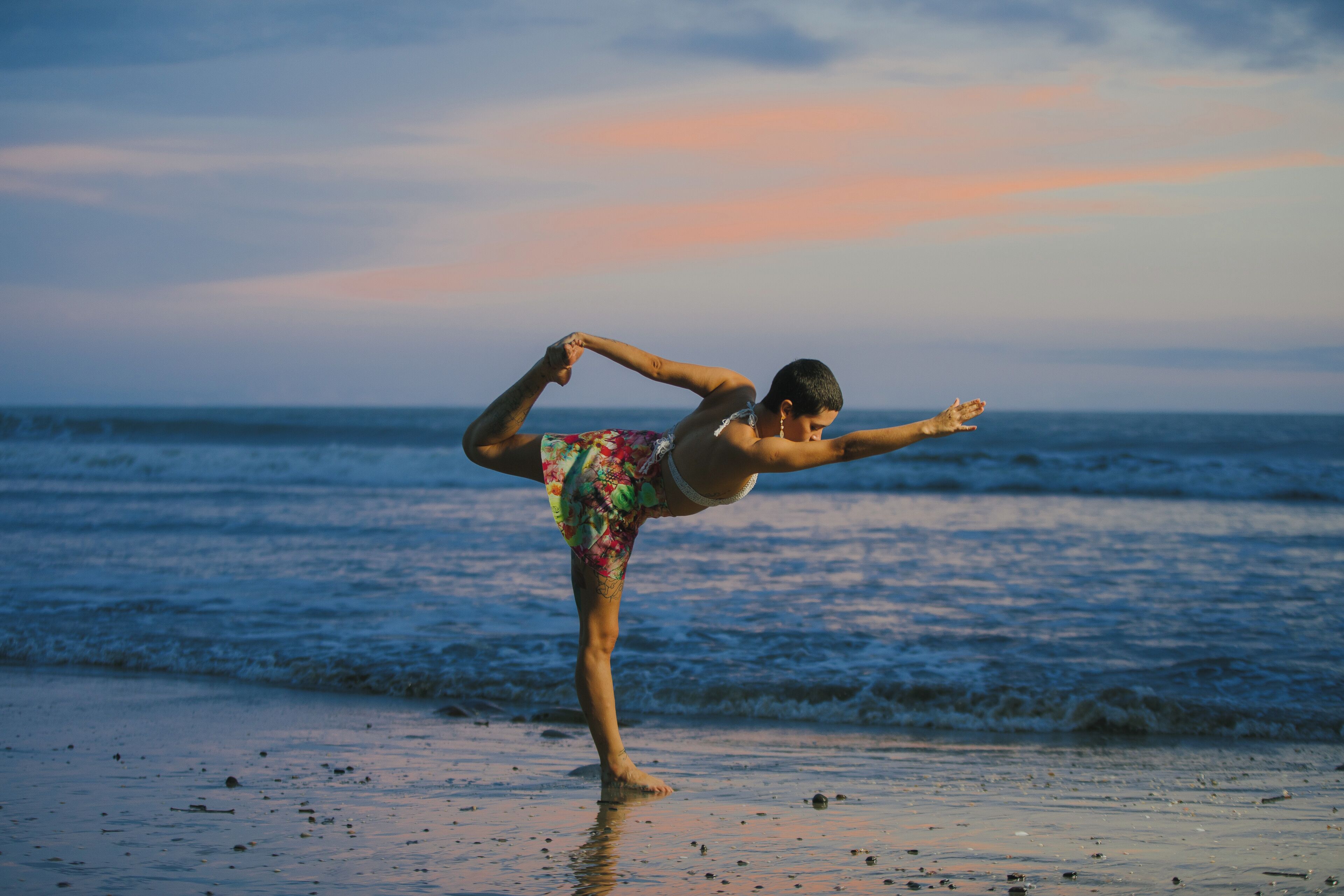 A person performing a yoga pose on a beach with the ocean in the background.