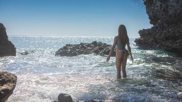 A person standing in shallow water near rocky cliffs.