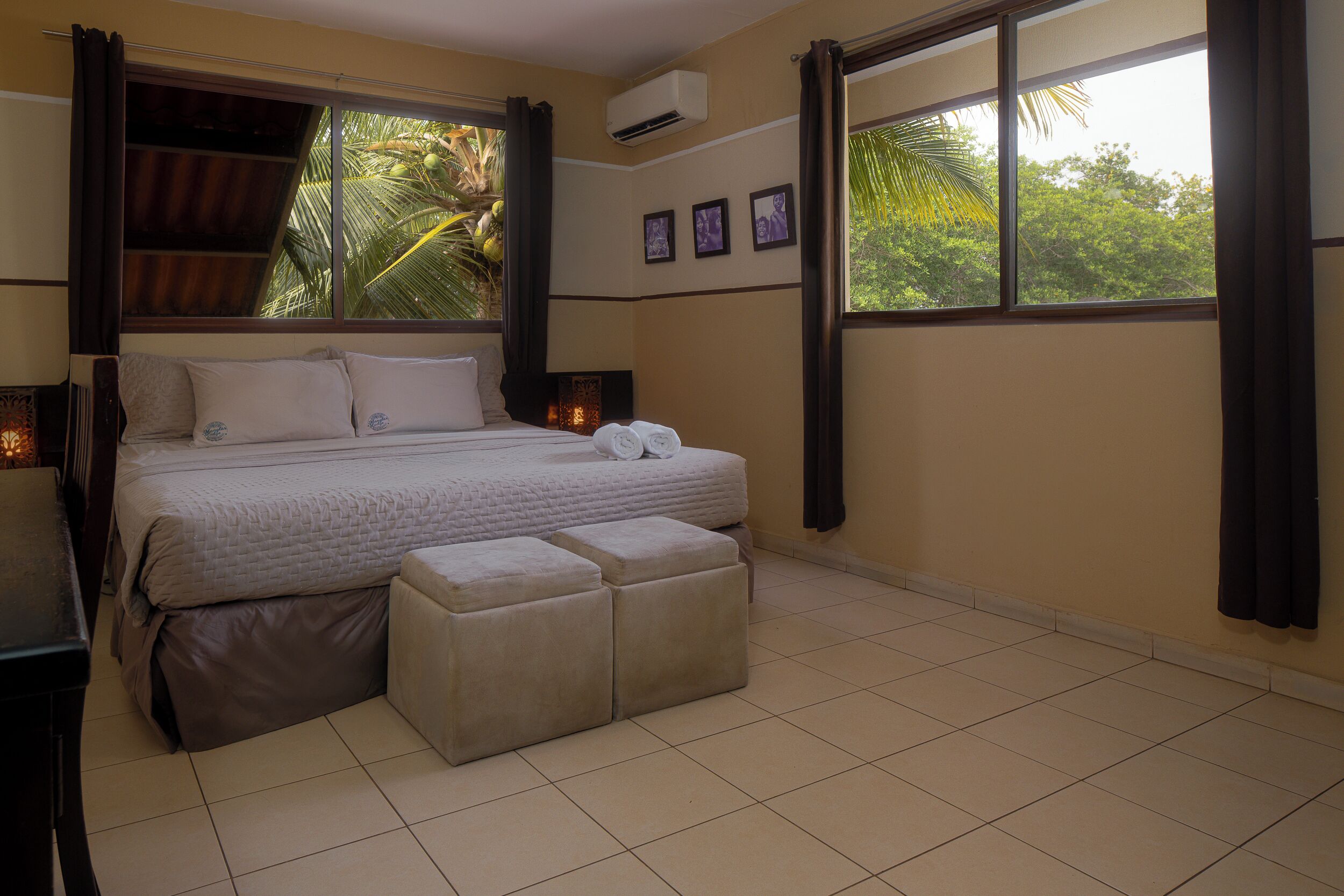 A bedroom with a bed, bedside tables, a window with curtains, and a wall-mounted air conditioner.