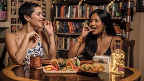 Two people dining at a table with a variety of dishes, a bottle, and a string of lights in the background. - Manglar Lodge (San Carlos)