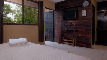A bedroom with a large bed, a TV mounted on a wooden wall, and a view of the outdoors.
