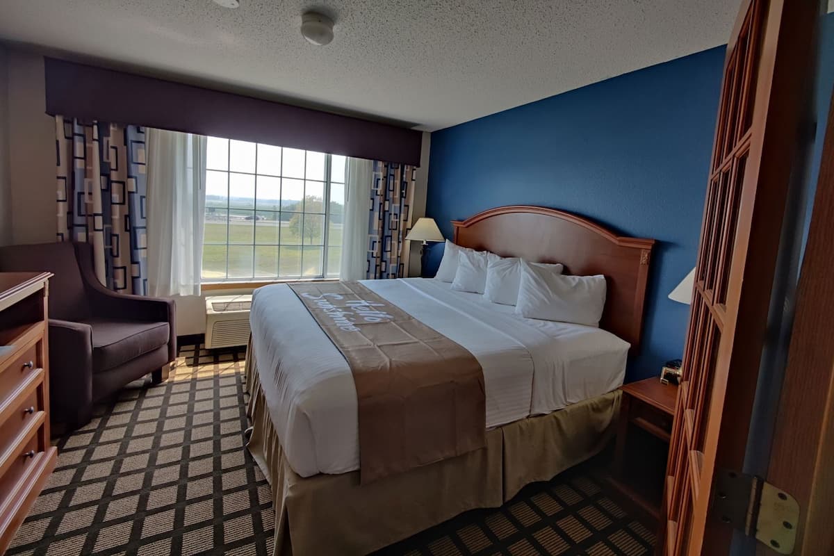 A hotel room with a large bed, a desk, a chair, a window with a view, and a patterned floor.