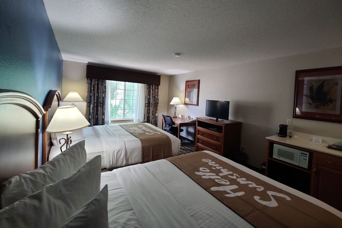 A hotel room with two beds, a desk, a television, and a microwave.