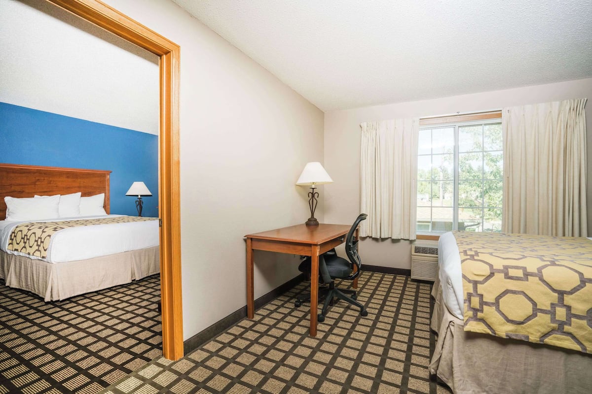 A hotel room with a bed, a desk, and a chair. There is a window with curtains and a view of trees outside.