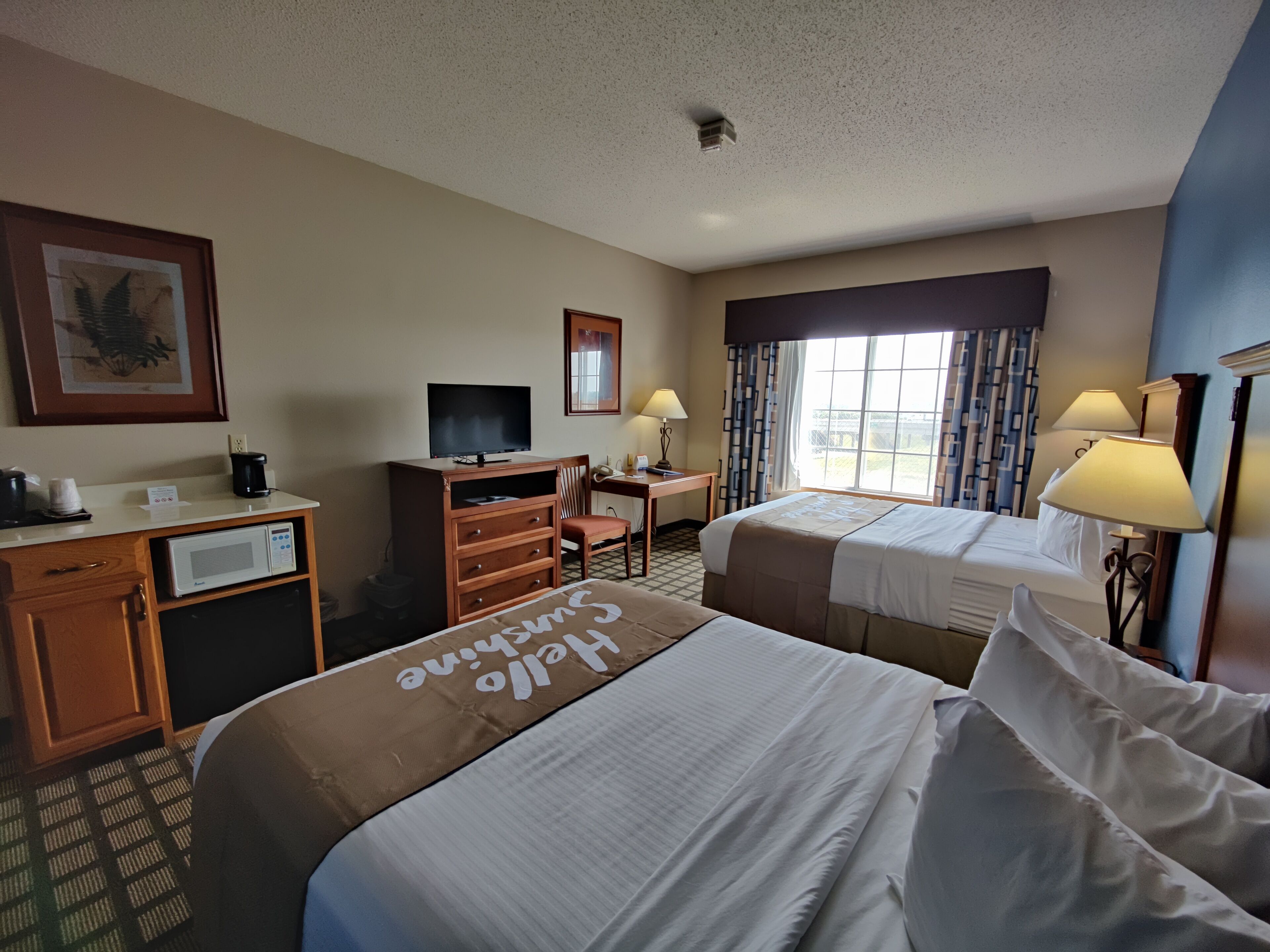 A hotel room with two beds, a desk with a computer, a television, and a window with curtains.