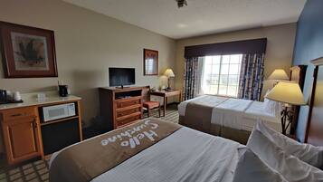 A hotel room with two beds, a desk with a computer, a television, and a window with curtains.