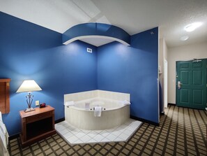 Un baño con una bañera grande, una mesita de madera con una lámpara y una puerta verde.