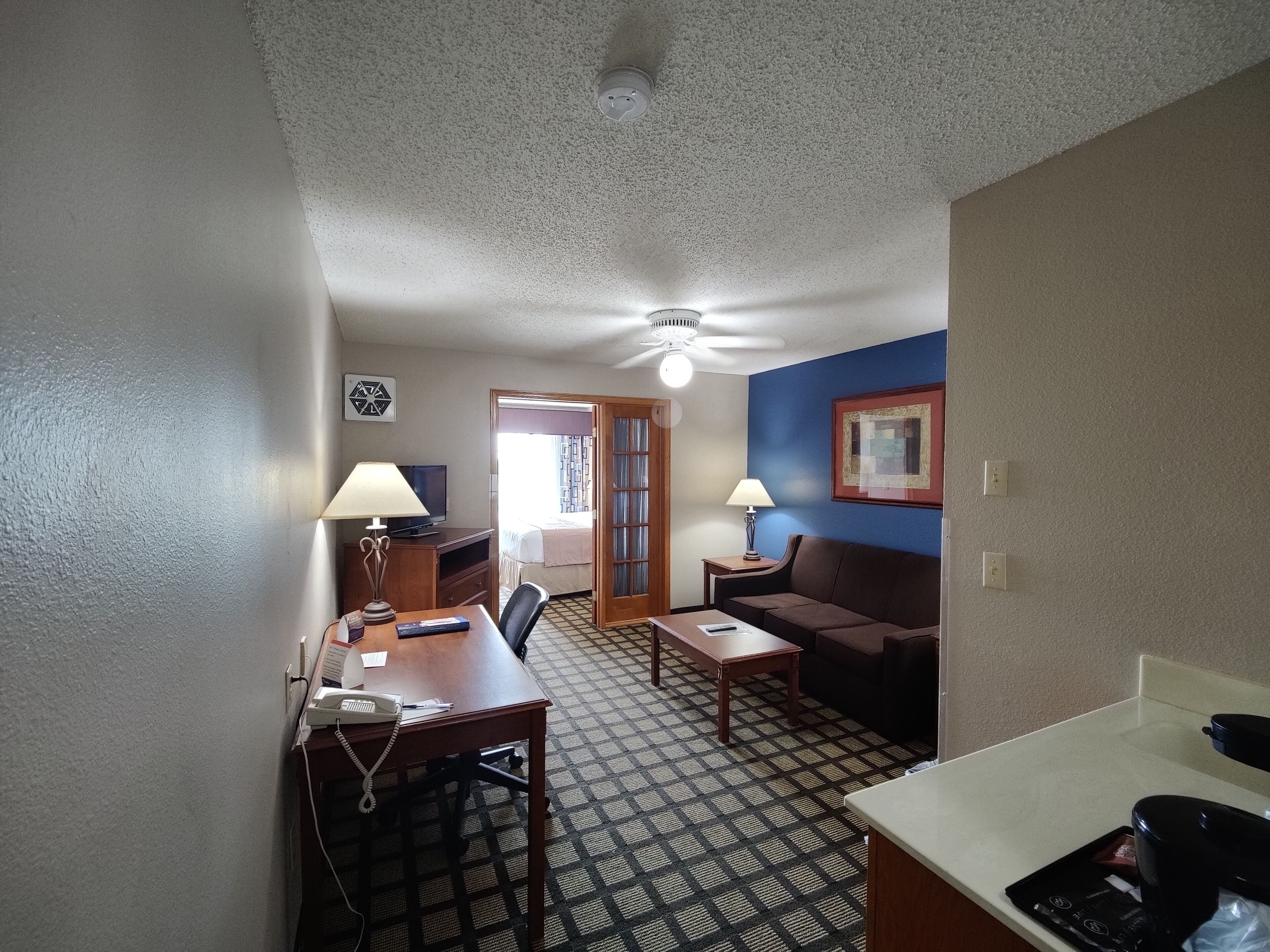 A compact hotel room with a kitchenette, a dining area, a sofa, and a bed.