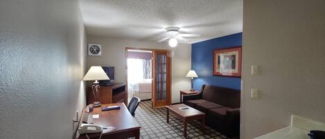 A compact hotel room with a kitchenette, a dining area, a sofa, and a bed.