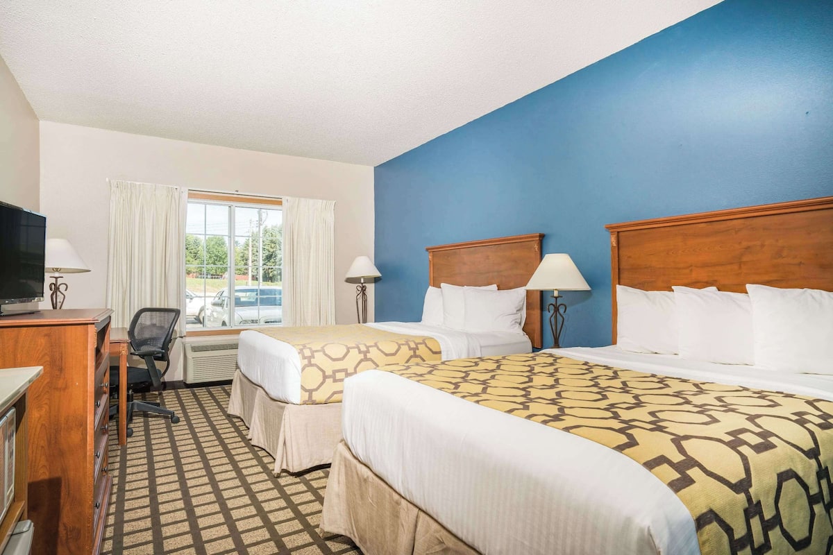 A hotel room with two beds, a desk, a chair, and a television.