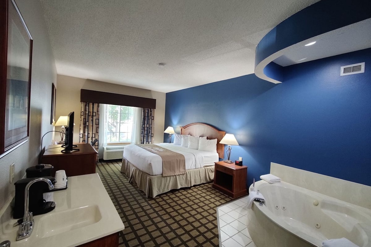 A hotel room with a bed, a desk with a computer, a sink, a bathtub, and a window with curtains.