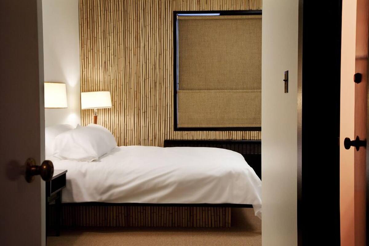 Une chambre d’hôtel avec un lit, des lampes de chevet, une fenêtre avec des stores et un panneau mural en bois.