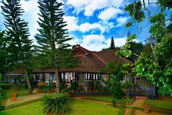 A traditional house with a tiled roof, surrounded by lush greenery and tall trees. - KTDC Lake Palace Thekkady (Peermade)