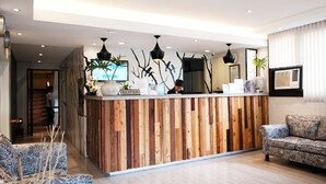 A reception area with a wooden reception desk, a sofa, and a potted plant. - Fersal Hotel (Quezon City)