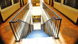 A multi-level interior with a central staircase flanked by railings, leading to a landing area with a patterned floor. - Fersal Hotel (Quezon City)