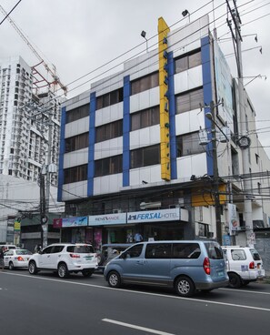 A multi-story building with a prominent yellow vertical sign, several ground-floor commercial establishments including a hotel, and a busy street with parked cars. - Fersal Hotel (Quezon City)
