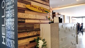A reception desk with a wooden panel wall, a sign with multiple languages, and a vase with flowers. - Fersal Hotel (Quezon City)