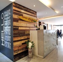 Un mostrador de recepción con un panel de madera, un letrero en varios idiomas y un jarrón con flores.