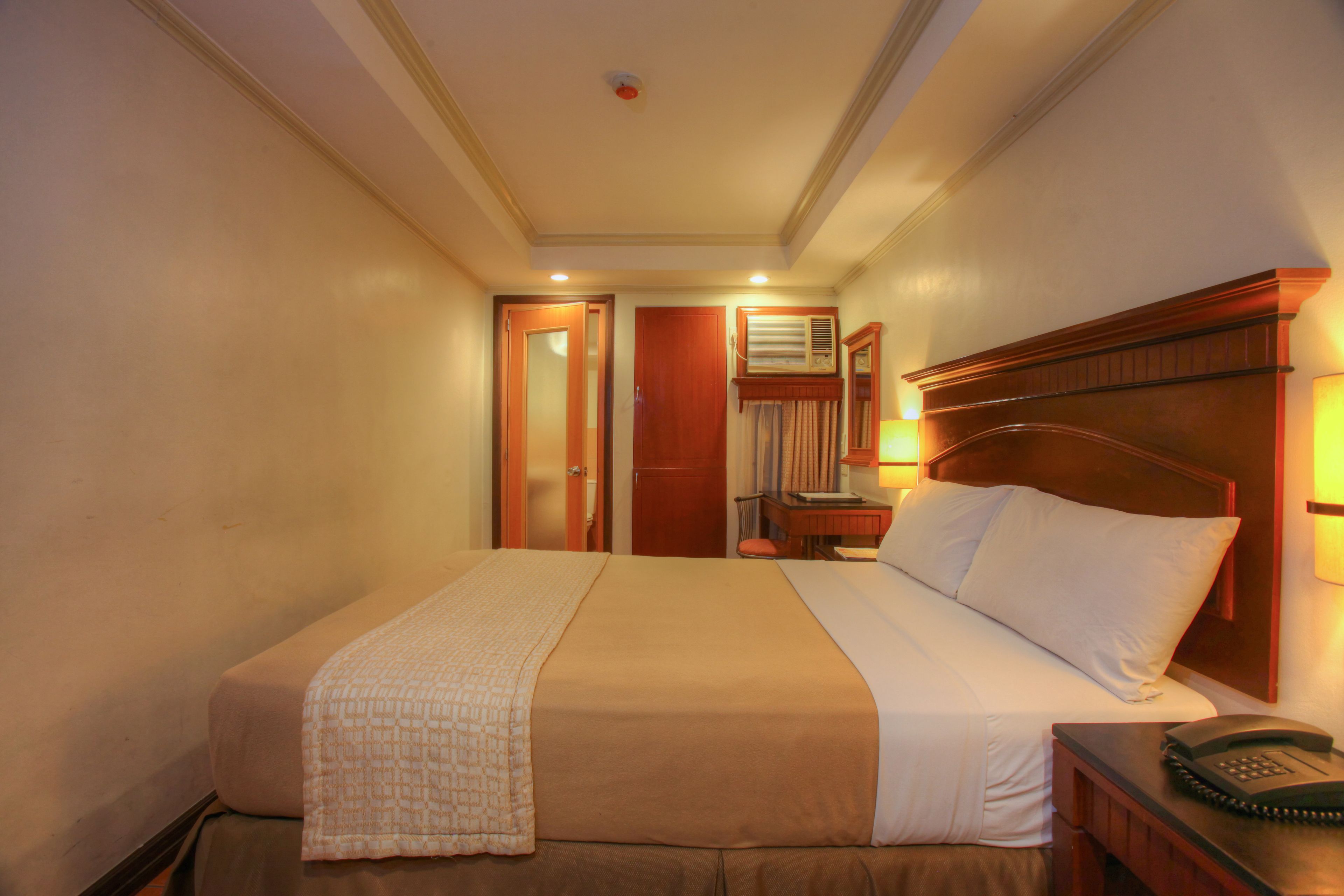 Una habitación de hotel con una cama grande, una mesita de noche con lámpara y un teléfono.