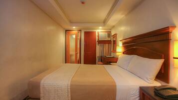 Una habitación de hotel con una cama grande, una mesita de noche con lámpara y un teléfono.