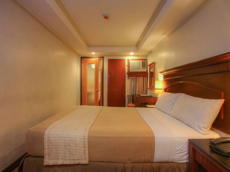 Una habitación de hotel con una cama grande, una mesita de noche con lámpara y un teléfono.