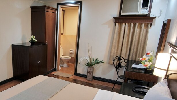 A hotel room with a bed, a desk, a chair, a wardrobe, a bathroom visible through an open door, a potted plant, and a mirror. - Fersal Hotel (Quezon City)