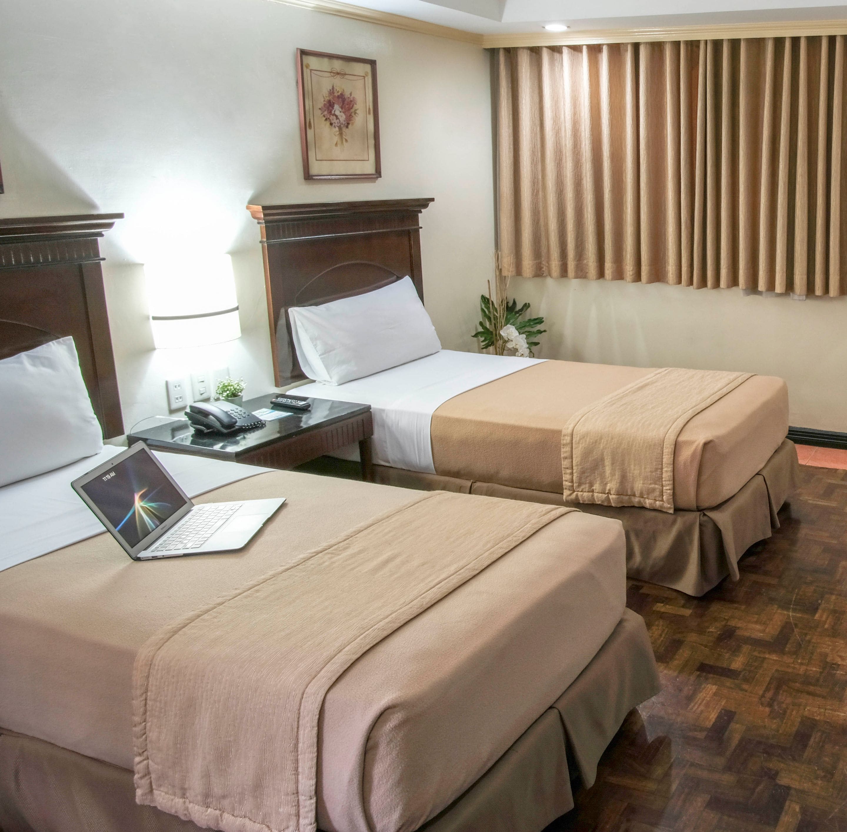 Une chambre d’hôtel avec deux lits, un bureau avec un ordinateur portable, une table de chevet et une fenêtre avec des rideaux.